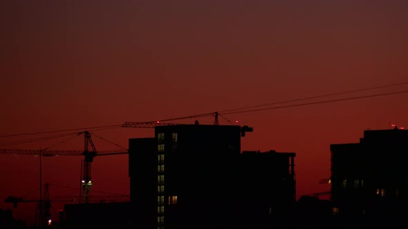 Timelapse. Silhouette of Working High Tower Crane on a Construction Site Against a Cloudless Sunset