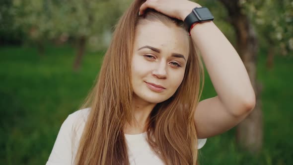 A Young Girl Smiles and Looks at the Camera While Fixing Her Hair