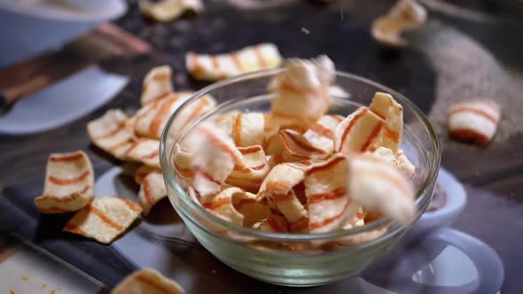 Appetizing Yellow Fried Potato Chips with Bacon Falling Into Glass Bowl on Table