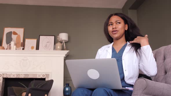 Friendly Female Black Clinician in White Gown Using Laptop for Remote Patient Consultation