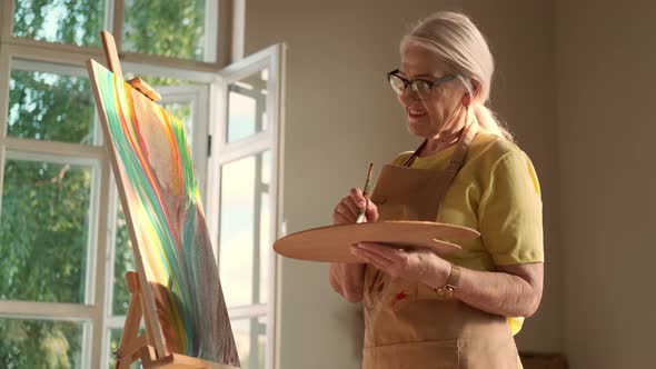 Senior Woman Artist Paints a Picture on Canvas