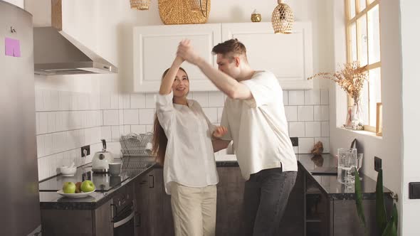 Happy Young Caucasian Married Couple Enjoy Dancing at Home in Kitchen.