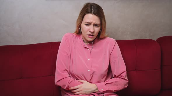 Stressed Young Woman Lying on Sofa Embracing Belly Suffering From Stomachache