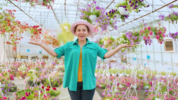 Standing in a Greenhouse with Indoor Plants Young Woman Florist Smiles Happy and Spreads Her Arms