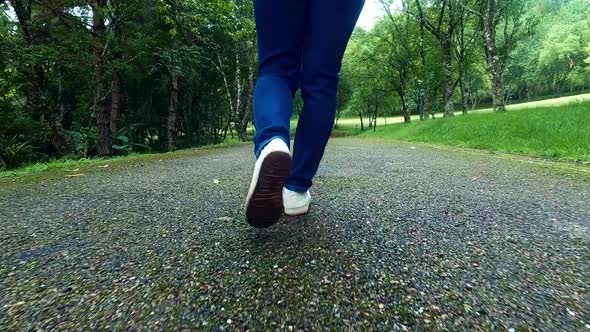 Close up of female traveler legs walking on asphalt road among nature around.