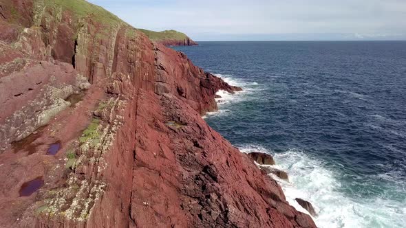 Drone ariel footage of red Welsh cliffs with blue sky's and crashing waves