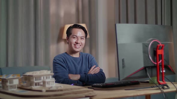 Engineer With House Model Smiling And Crossing His Arms To The Camera While Working On A Desktop