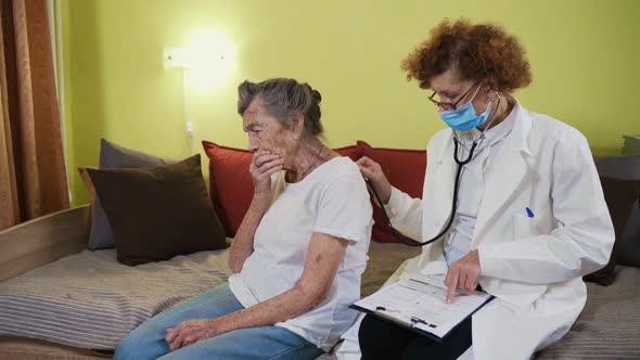 Elderly Female Doctor in White Lab Coat Medical Mask Makes Medical Examination of Senior Woman at