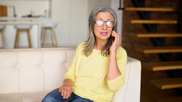 Portrait of Charming Senior Woman Talking on Smartphone Sitting on the Sofa