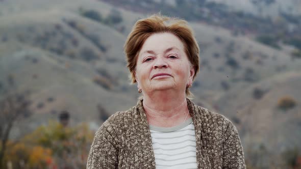 Portrait of an Elderly Woman Against the Background of an Autumn Mountain Landscape