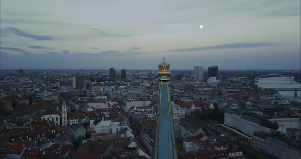 Flying backwards from Crown on St. Martin Church tower in Bratislava at twilight with moon in backgr