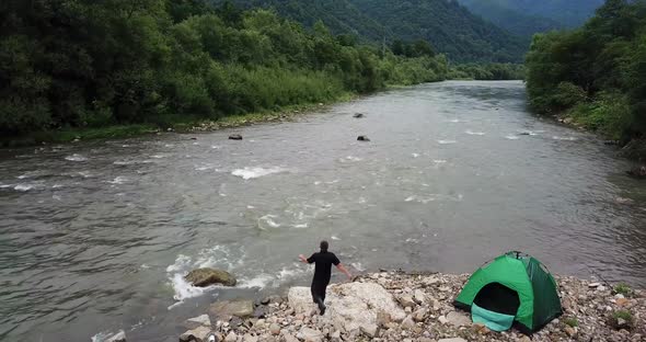 A Fisherman Fishes By Spinning a View of a Mountain River and a Green Tent