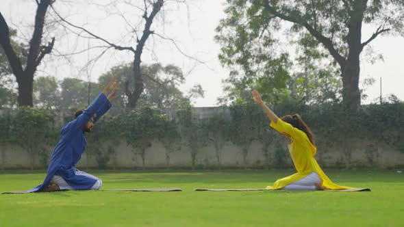 Extended Child Yoga Pose or Prasarita Balasana is being done by an Indian couple in an Indian outfit