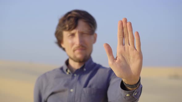 A Man Standing in a Desert Holds an Open Palm in Front of Him As a Stop Sign