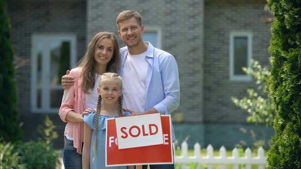 Happy Family Holding Sold Sign, Standing Against New Bought House, Thumbs Up