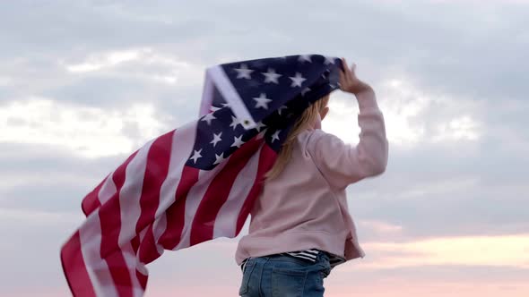 Back View Blonde Girl Waving National USA Flag Outdoors Over Sunset Sky at Summer on Beach American