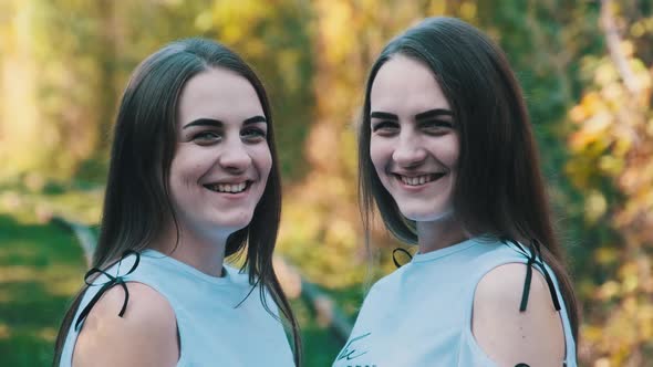 Twins Girls Smiling and Look at Camera in Green Nature Background