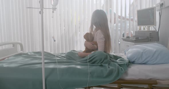 Preteen Girl Patient Hugging Teddy Bear Sitting on Bed in Hospital