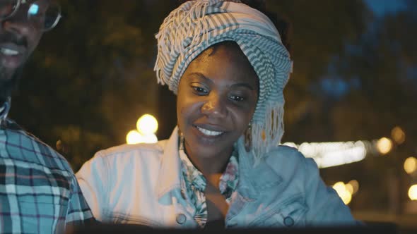 Afro Man and Woman Using Laptop and Talking Outdoors in Evening