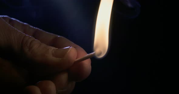 Slow motion macro footage of a white candle lit by a match on a dark background