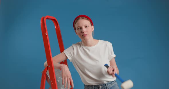 Young Woman Stands with a Stepladder Holding a Hammer in Her Hand on Blue Background