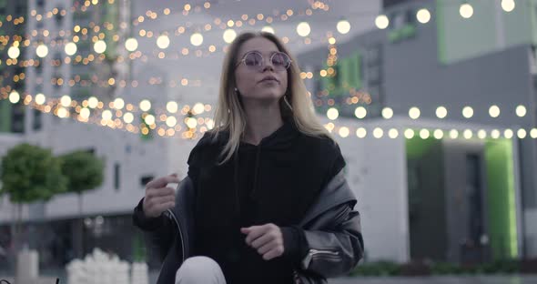 Young Pretty Girl Smiling and Posing on Camera, Near a Modern Residential Area, Evening in the City