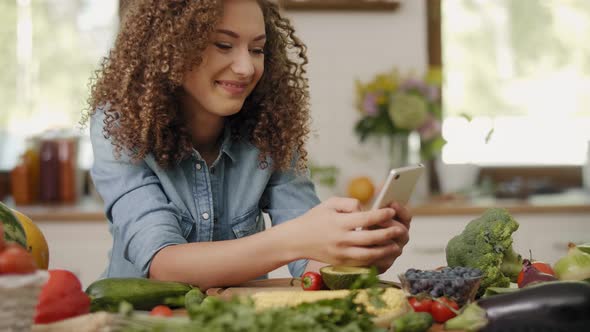 Smiling woman with mobile phone in the kitchen