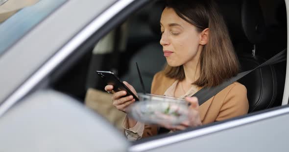 Woman Typing on a Smart Phone While Having a Snack in a Vehicle