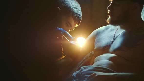 Tattoo Session Under Lamp Light with Customers Shoulder Arm By Male Tattooist