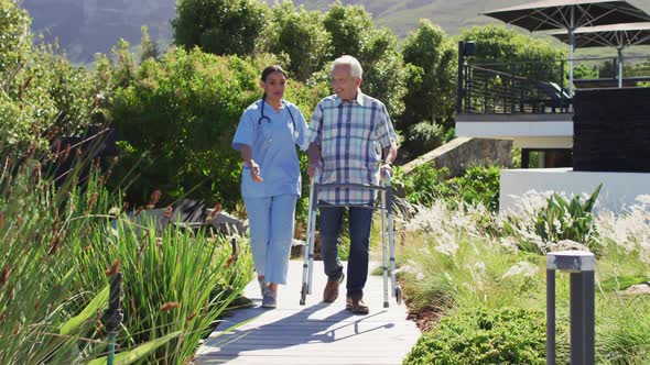 Video of happy biracial female doctor taking care of caucasian senior man in rest home garden