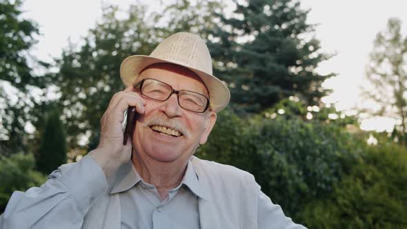 Portrait of Happy Senior Man Talking on the Phone in Sunny Park with Joy