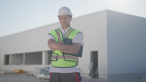 Zoom in to Serious Confident Professional Caucasian Man in Uniform and Hard Hat with Crossed Hands