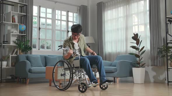 Asian Man Sitting In A Wheelchair And Exercising With Dumbbell At Home