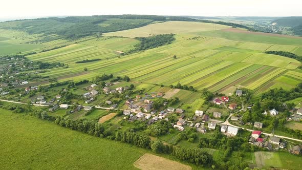 Aerial view of small village with small houses among green trees with farm fields and distant 