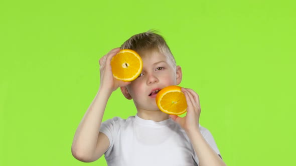 Little Boy Holds an Orange Slice and Makes Various Grimaces. Green Screen