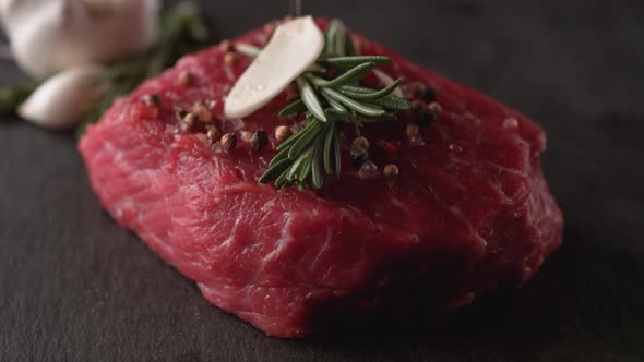 Camera follows putting herbs and spices on raw steak meat. Slow Motion.