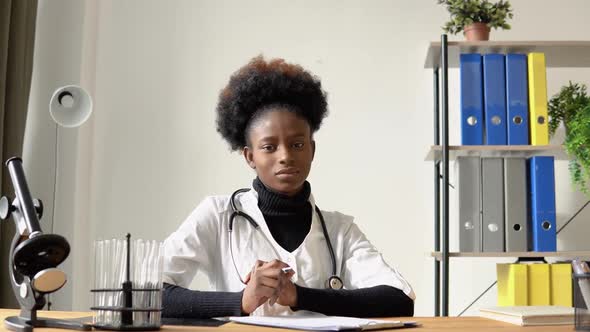 African American Female Doctor Looking at Camera While Sitting at Table in Hospital