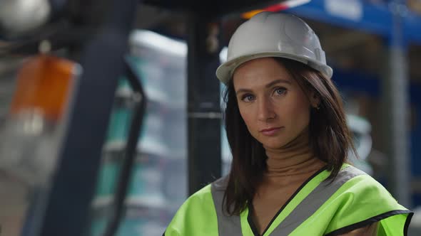 Beautiful Young Caucasian Woman in Hard Hat Sitting in Forklift Looking at Camera Smiling