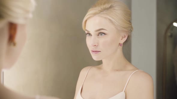 Close-up Reflection of Beautiful Blond Caucasian Woman with Grey Eyes Looking at Mirror and Smiling