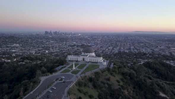 Aerial orbit of Griffith Observatory and Los Angeles city skyline seen in the distance.