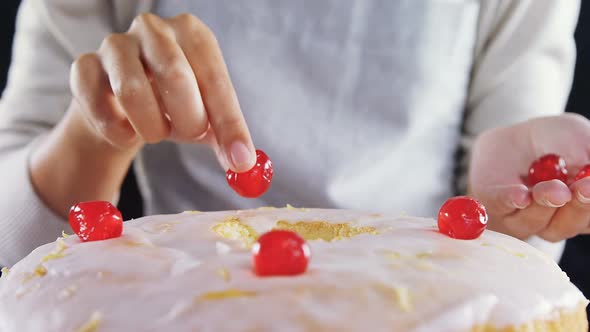 Woman topping a fresh baked cake with cherry