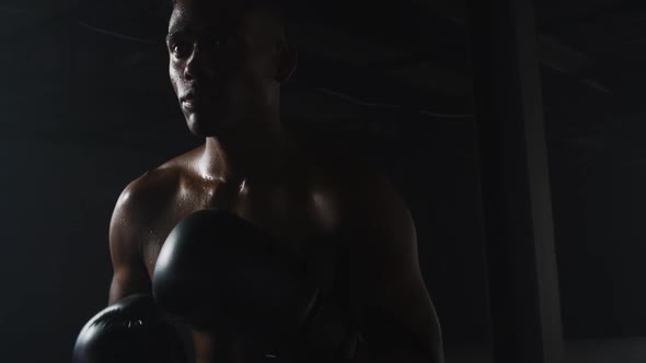 African american man wearing boxing gloves banging fists together in dark room