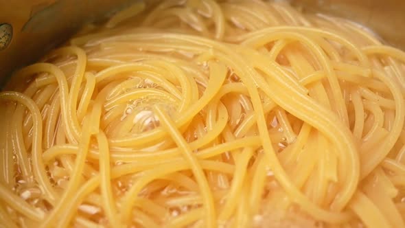 Raw spaghetti is being cooked in boiling water in a kitchen pot.