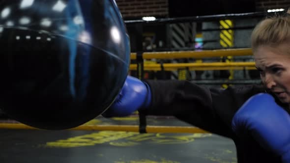 A Beautiful Young Woman in Blue Boxing Gloves Hits a Punching Bag in the Gym