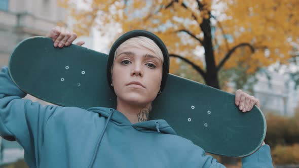 Young Caucasian Woman Skater Holding Skateboard Behind Her Head in the Park in Autumn