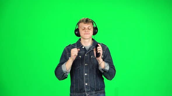 Young Man in Big Headphones Goes, Listening Music and Dancing with Smartphone on Green Screen at