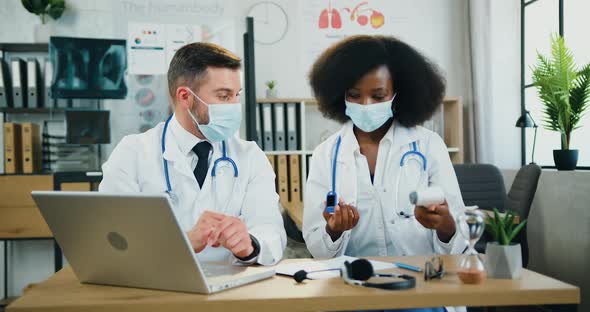 Two Mixed Race Doctors in Protective Masks Remotely Supporting their Patient During Video call