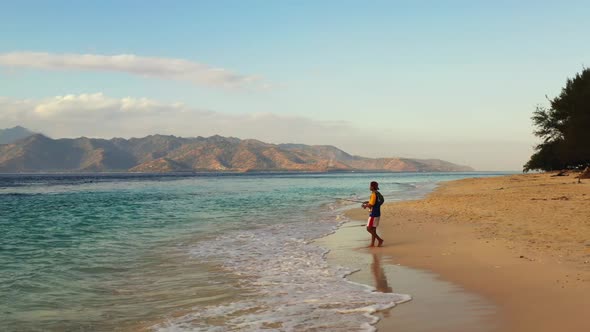 Man alone fishing alone on exotic island beach trip by blue water with bright sandy background of Gi