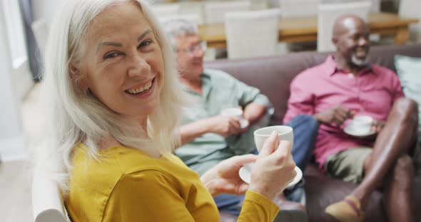 Animation of happy diverse female and male senior friends drinking coffee at home