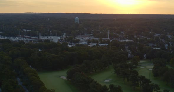 Forward Aerial of a Small Town Amongst Trees and Near a Golf Course at Sunset